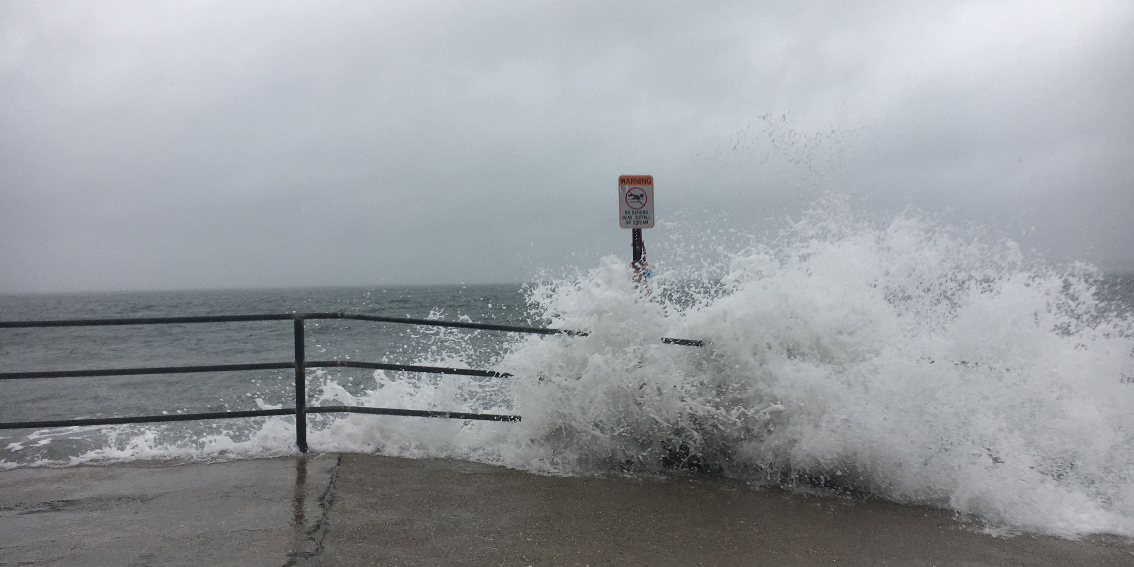 Waves breaking over railing overlooking the ocean on a stormy day