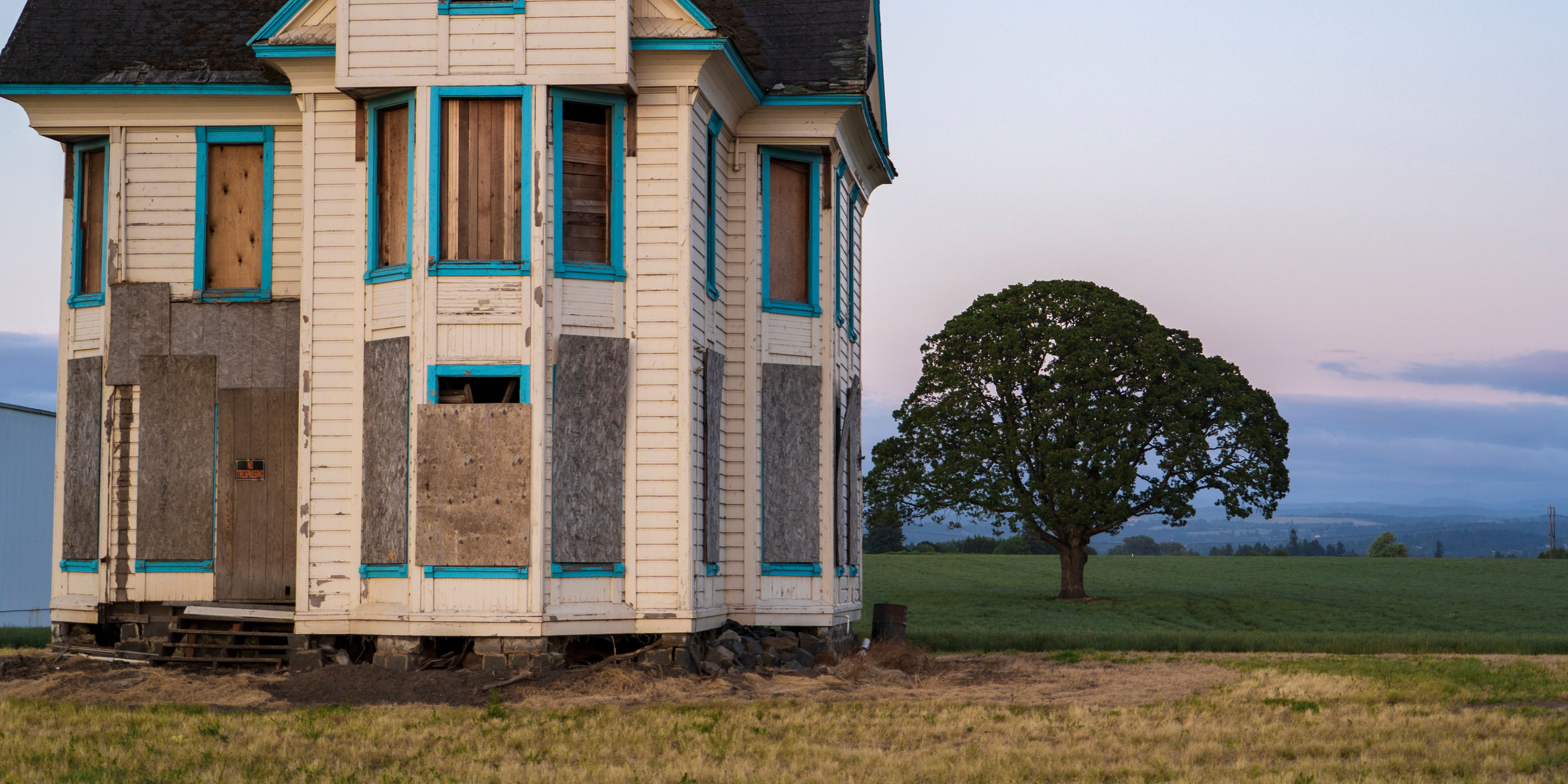 An abandoned, boarded-up house in a field.